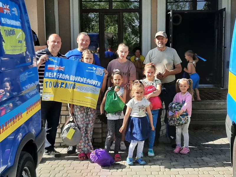 Volunteers and refugee families outside an aid centre in Ukraine, holding a banner from the aid convoy